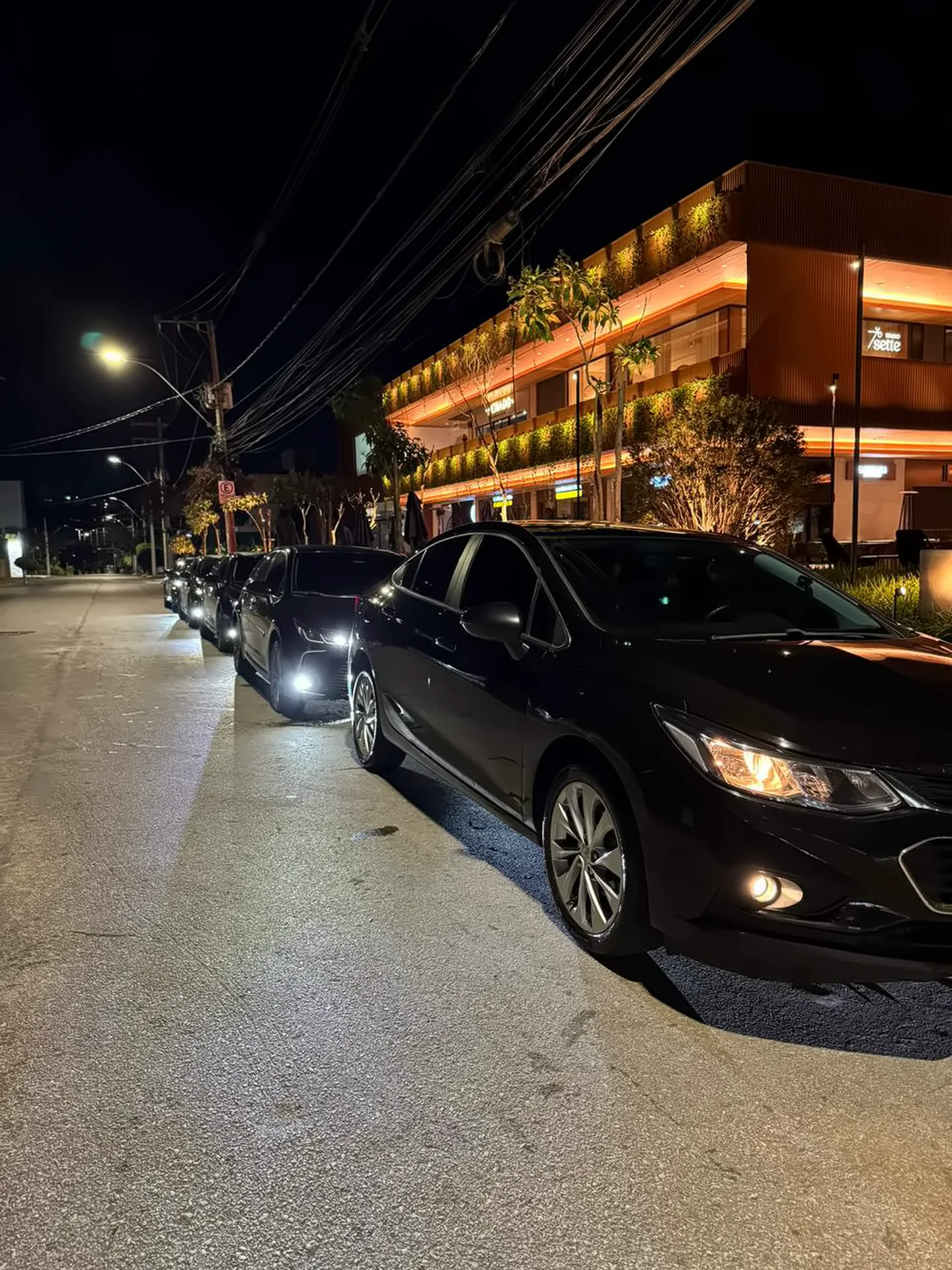 Frota de sedans executivos pretos da Elite enfileirados à noite com faróis acesos